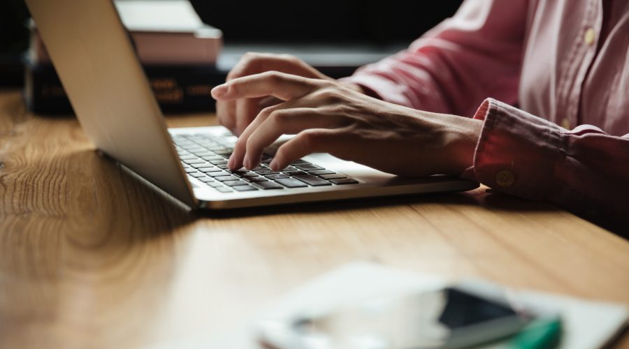 Cropped side view of woman sitting by the table in cafe and using laptop computer
